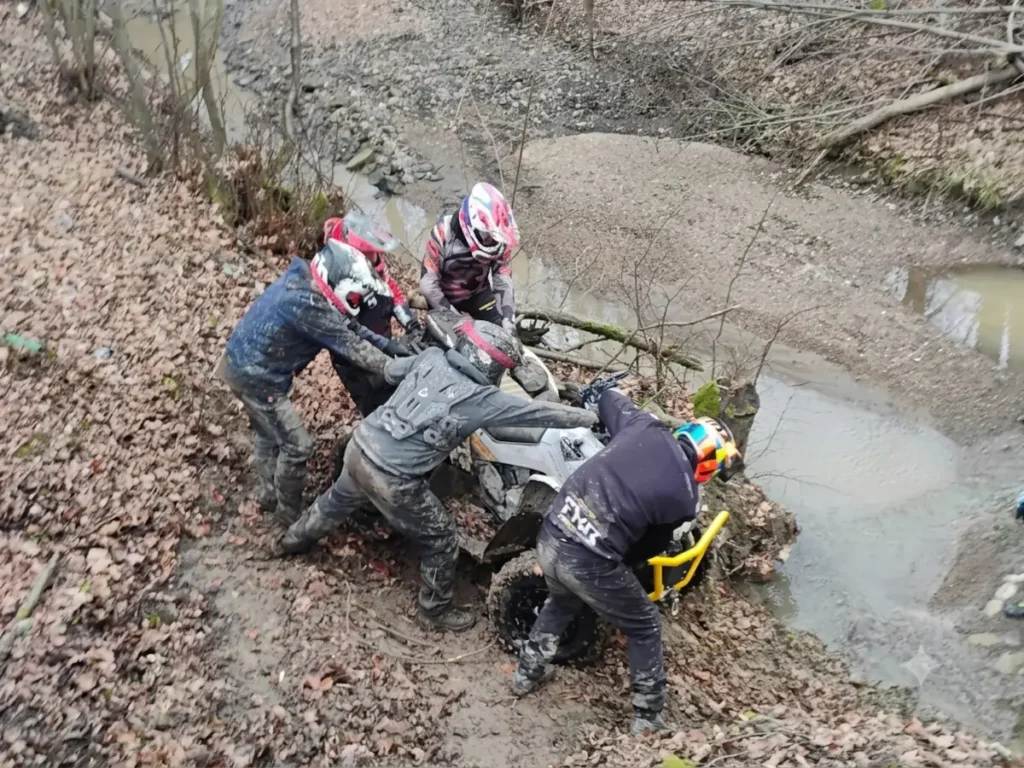 Quad w błocie wyciągany przez grupę ludzi na torze quadowym